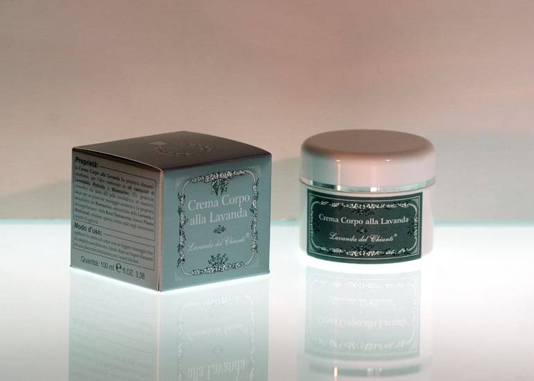 Plastic jar with gray label and the inscription: "Lavender body cream" placed on a lighted surface and nearby a silver box with the inscription "Lavanda del Chianti", pink-brown background