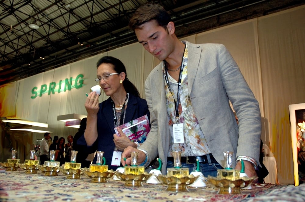 An ophthalmologist attentive to the olfactory analysis of a perfume chosen from a row of 8 glass bottles placed on a table. On the background curtain and the inscription: "spring"