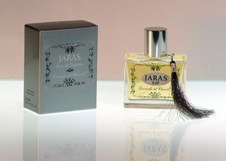 Perfume bottle in transparent glass with silver seal and cap with Jaras writing. Silver box with inscription: "Jaras Eau de Parfume" by "Lavanda del Chianti". Bright light background with reflection on the glass