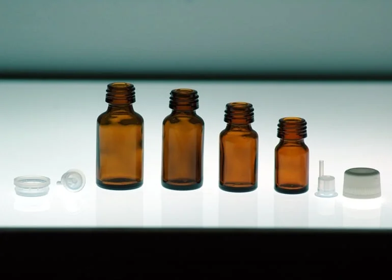 Flaconi di vetro farmaceutico giallo di varie capacità per contenere oli essenziali su sfondo luminoso bianco ed accessori plastici di chiusura
