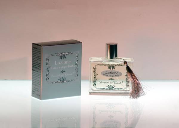 Flacone in vetro trasparente serigrafato con scritta "Lozione tonica e dopo barba da Lavanda del Chianti" con elegante guarnizione morbida argento e scatola argento su sfondo chiaro e riflessi sul piano di appoggio