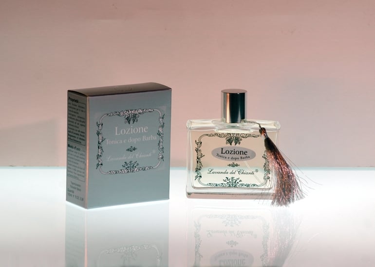 Transparent glass bottle silk-screened with the writing "Chianti lavender tonic and aftershave lotion" with elegant silver soft seal and silver box on a light background and reflections on the support surface