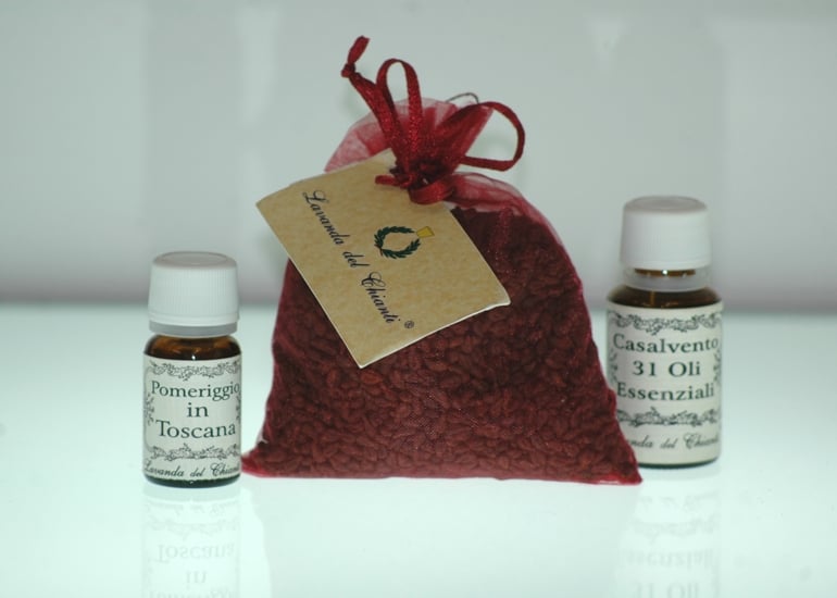 Sacchetto di organza color vinaccia con semi di uva e due flaconi farmaceutici in vetro giallo di profumo ambiente "Pomeriggioin Toscana" e "Casalveto 31 oli essenziali"; cartellino giallo con scritta: "Lavanda del Chianti". Sfondo bianco