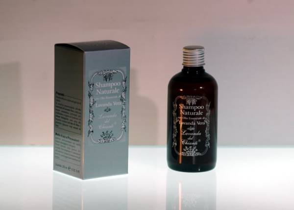 Brown plastic bottle with silver box on a light luminous surface and pink background. Silver framed writing "Lavender Vera natural shampoo" from "Lavanda del Chianti"